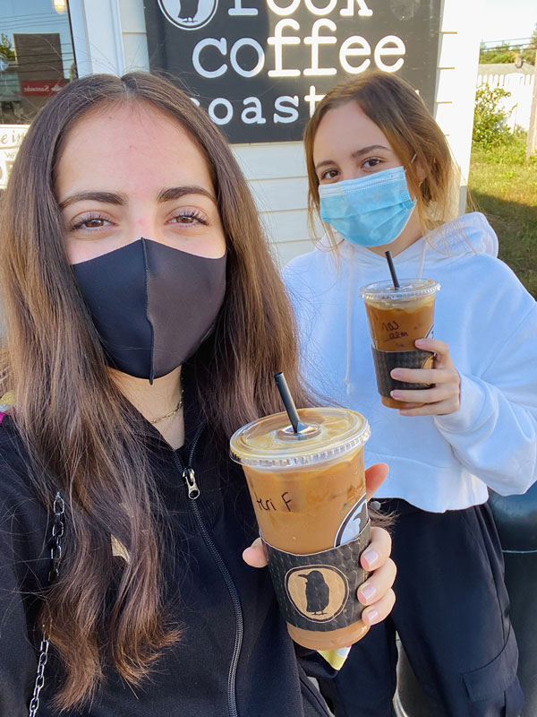 Two women holding iced coffees and wearing masks