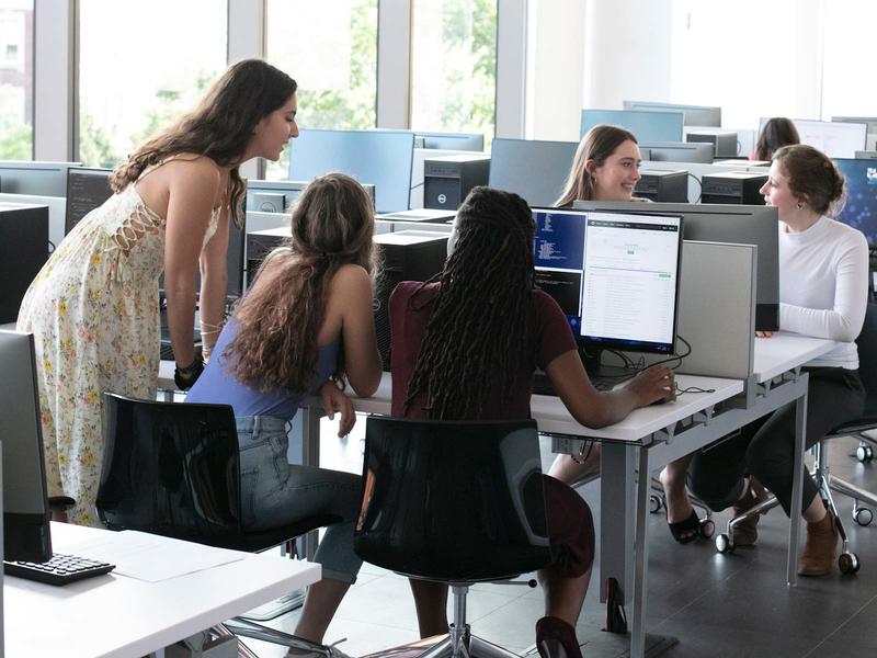 students huddled around a computer in a bright computer lab