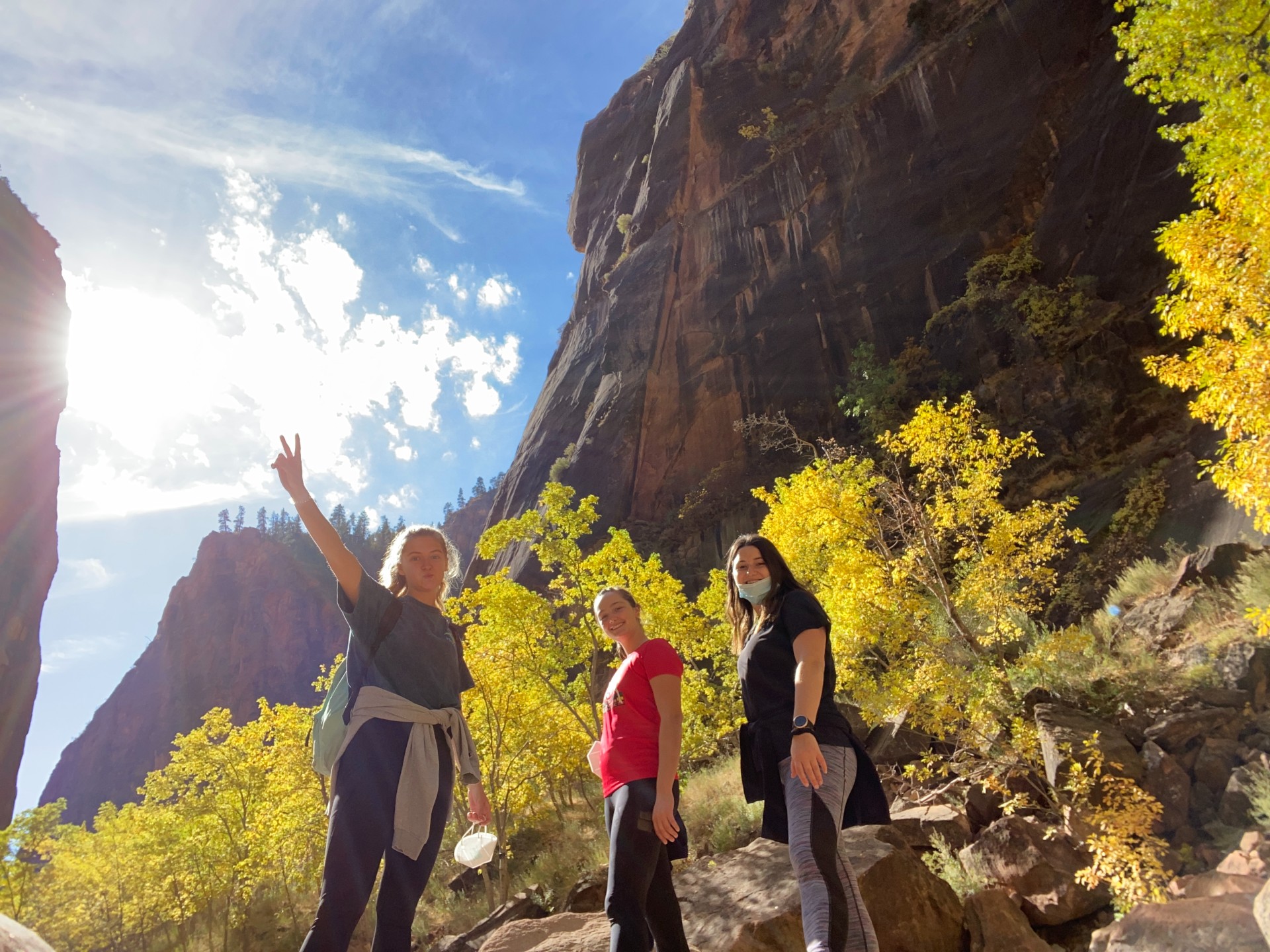 Three students hiking in rocky Utah with yellow tree leaves in background
