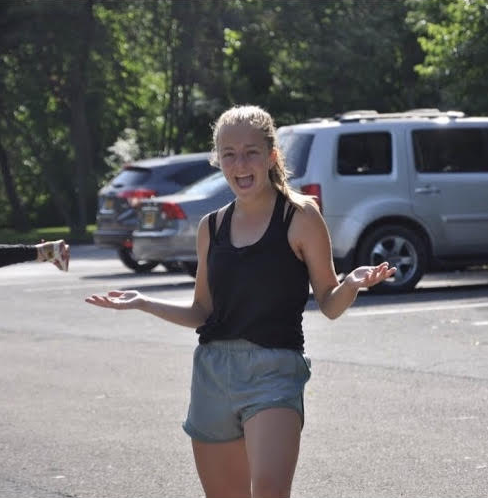 Student Evelyn Van Ness standing in a parking lot with her arms out in a sort of shrug pose.