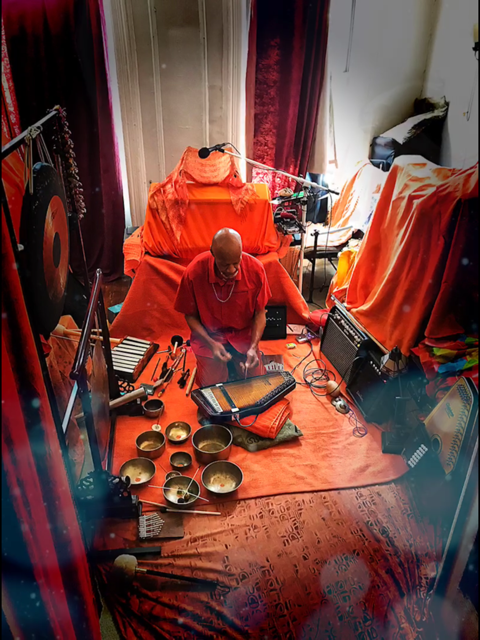 A man kneeling down on orange blankets surrounded by musical instruments