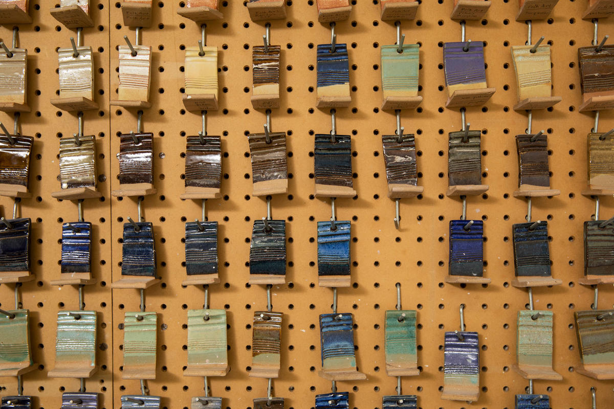 A variety of yellow, brown, blue, and green glazed ceramic tiles hang on a cork wall.