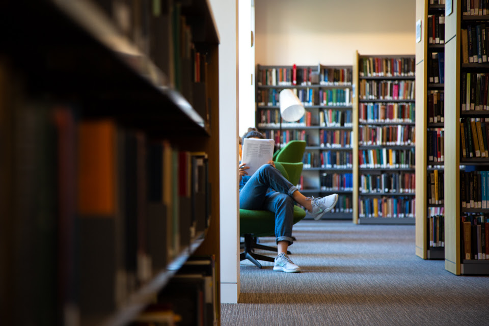 legs of a woman sitting in the library peeking out from behind stacks of books