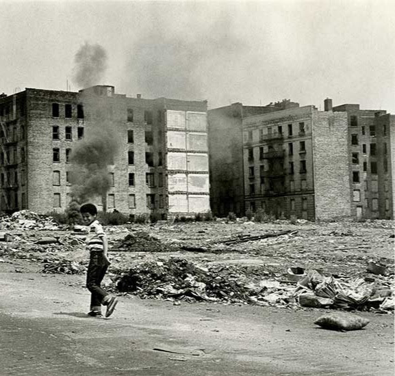 Young child looks at camera while standing in front of building ruins