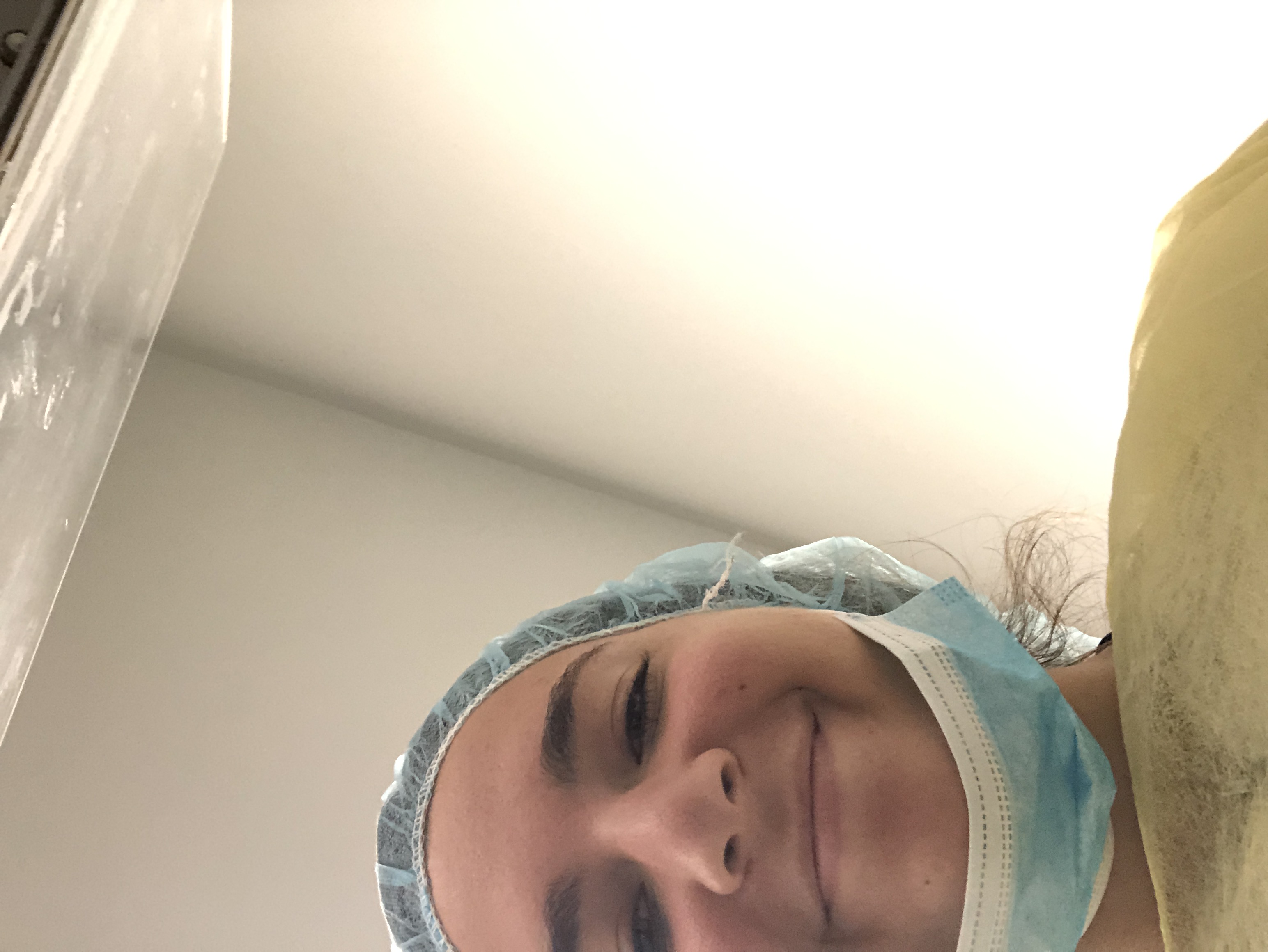 A selfie of Dandeneau in the lab, wearing a protective tarp, a hairnet, and a medical mask momentarily pulled down to show her smile