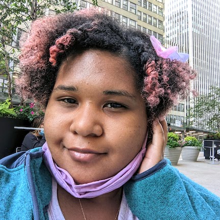 photo of a person with brown skin and black with pink streaks, lavender mask around their neck