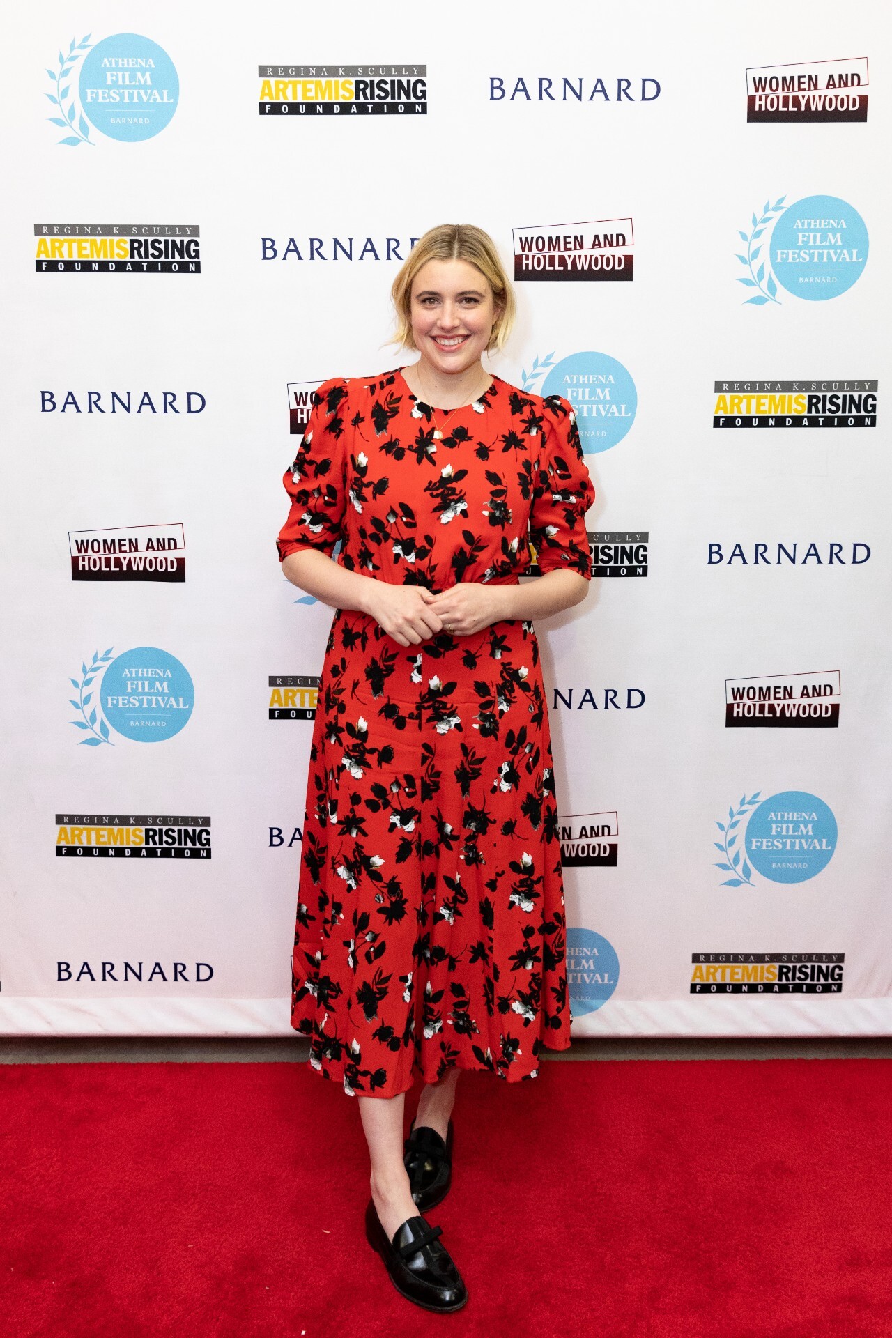 Greta Gerwig on the red carpet of the Athena Film Festival in 2020 — Gerwig stands against a photo backdrop with logos for Barnard and the film fest