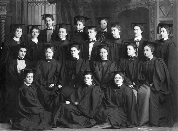 A class portrait from 1899, where a group of about 20 women pose in a group wearing graduation robes