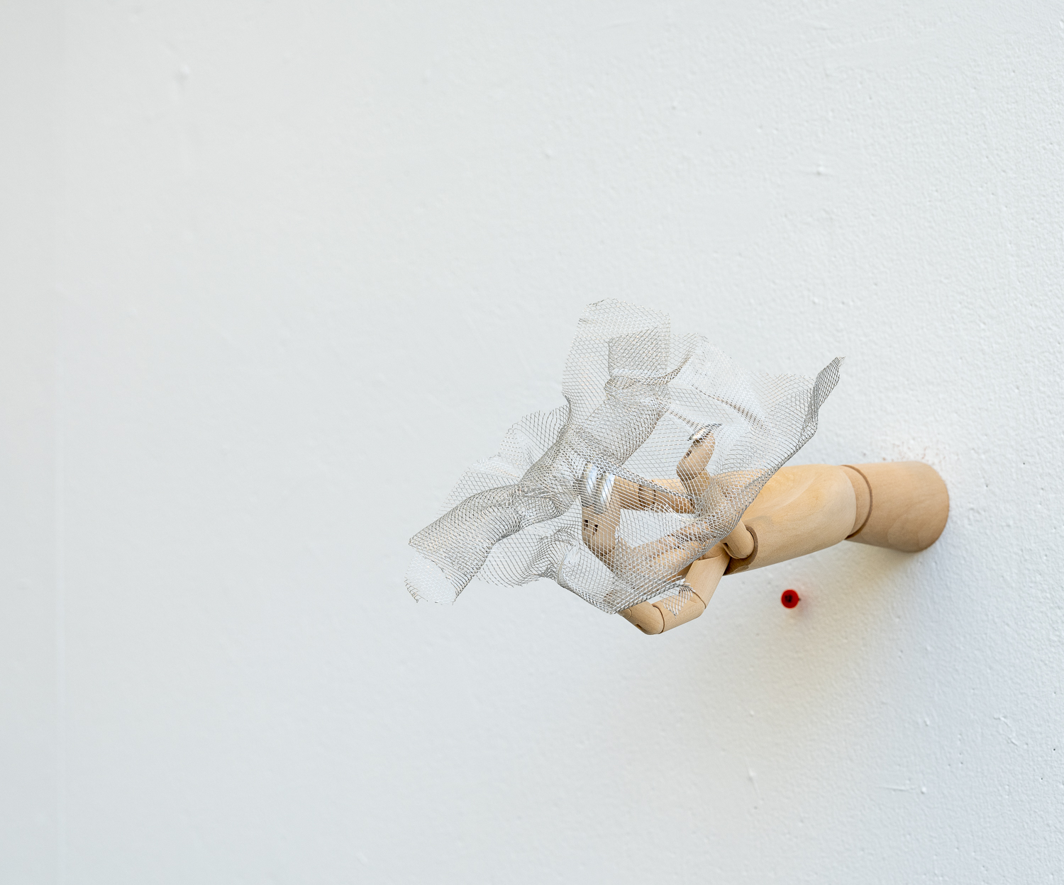 A wooden hand sticking out of the wall holds a crumpled piece of a mesh material