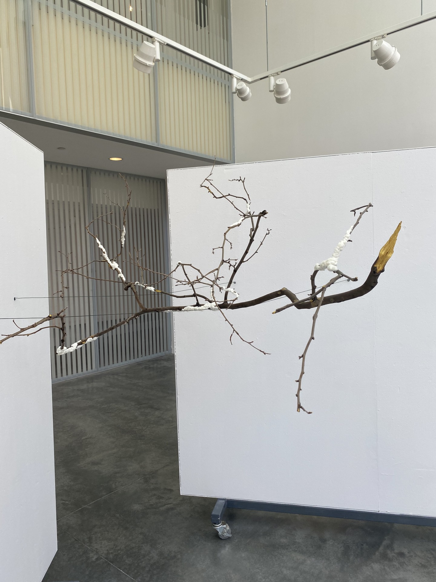 A hanging sculpture looks like a thin tree branch with some other objects hanging off it