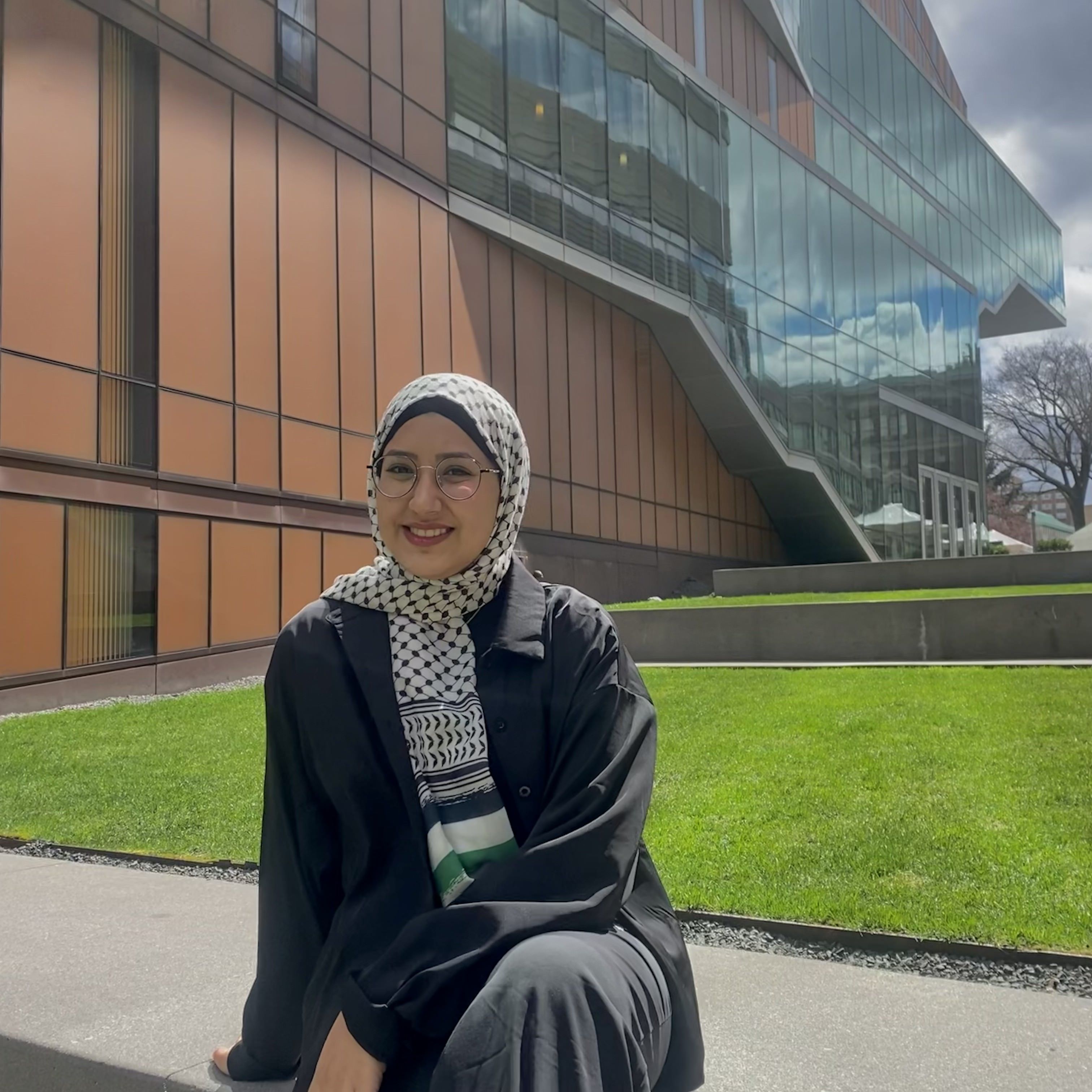 Aseel sitting in front of the Diana Center wearing black with a white patterned head scarf.