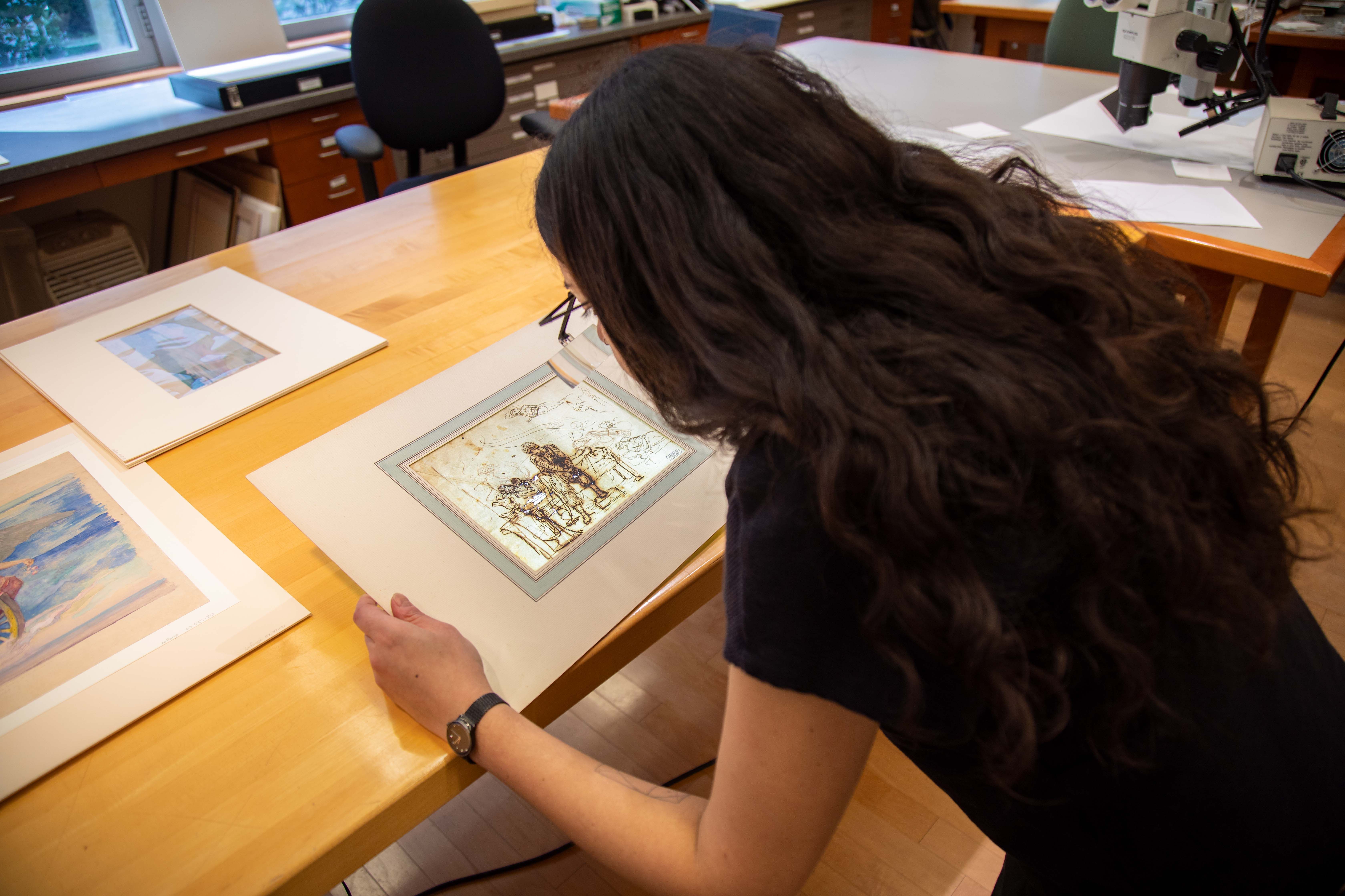 Loike pictured from behind in the paper conservation lab at the met studying a drawing.