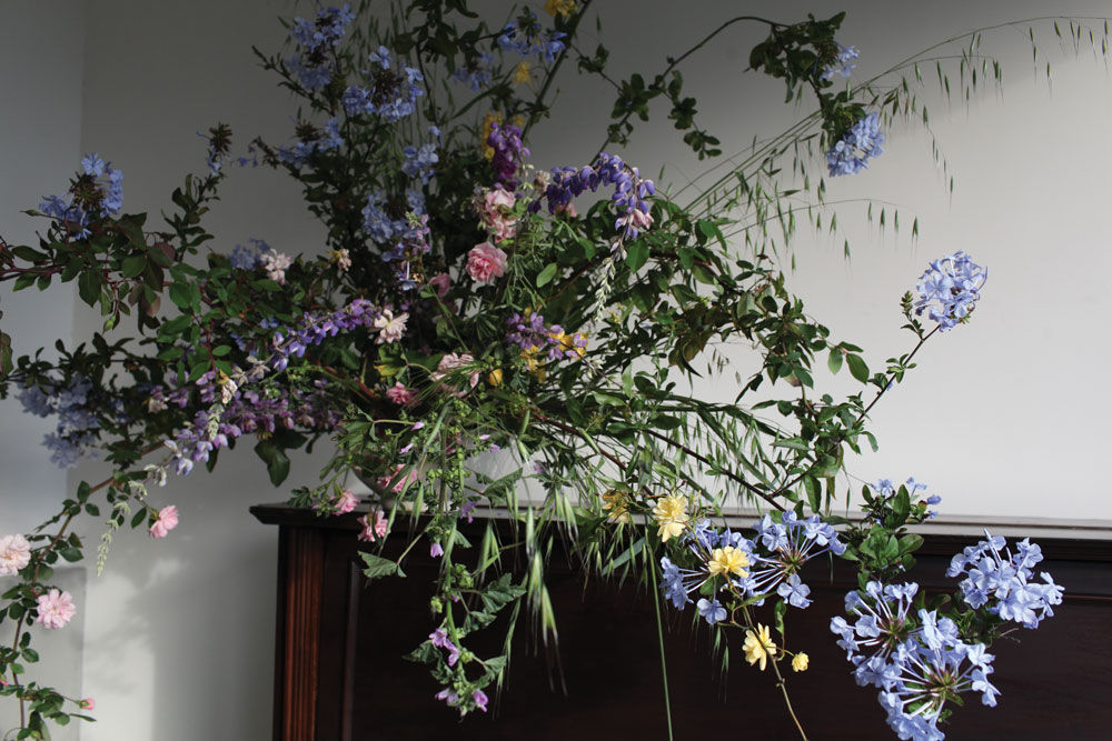 floral arrangement of purple, pink, and blue small flowers with arching leaves on branches