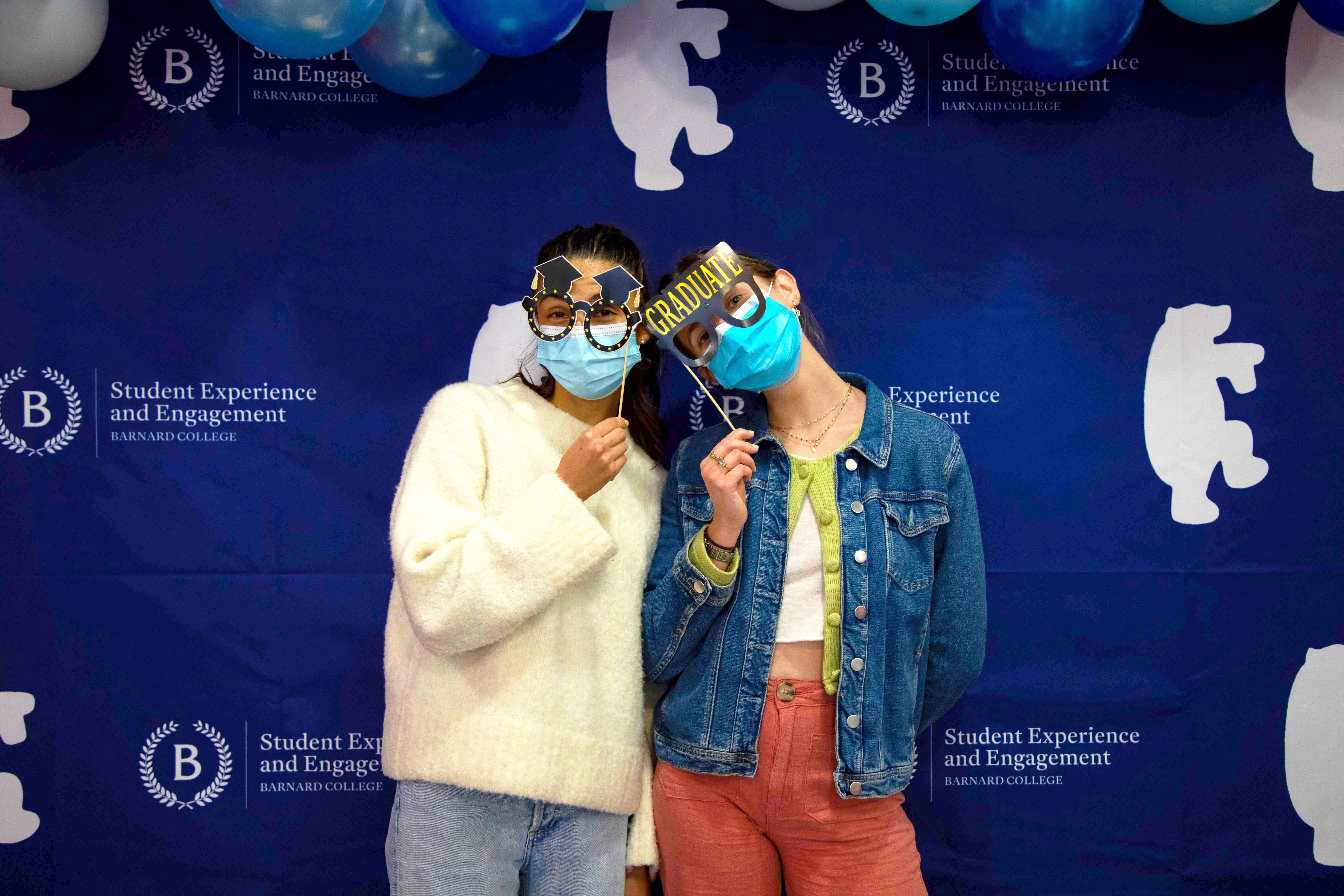 Two masked students post in front of a blue step and repeat with sunglass props.