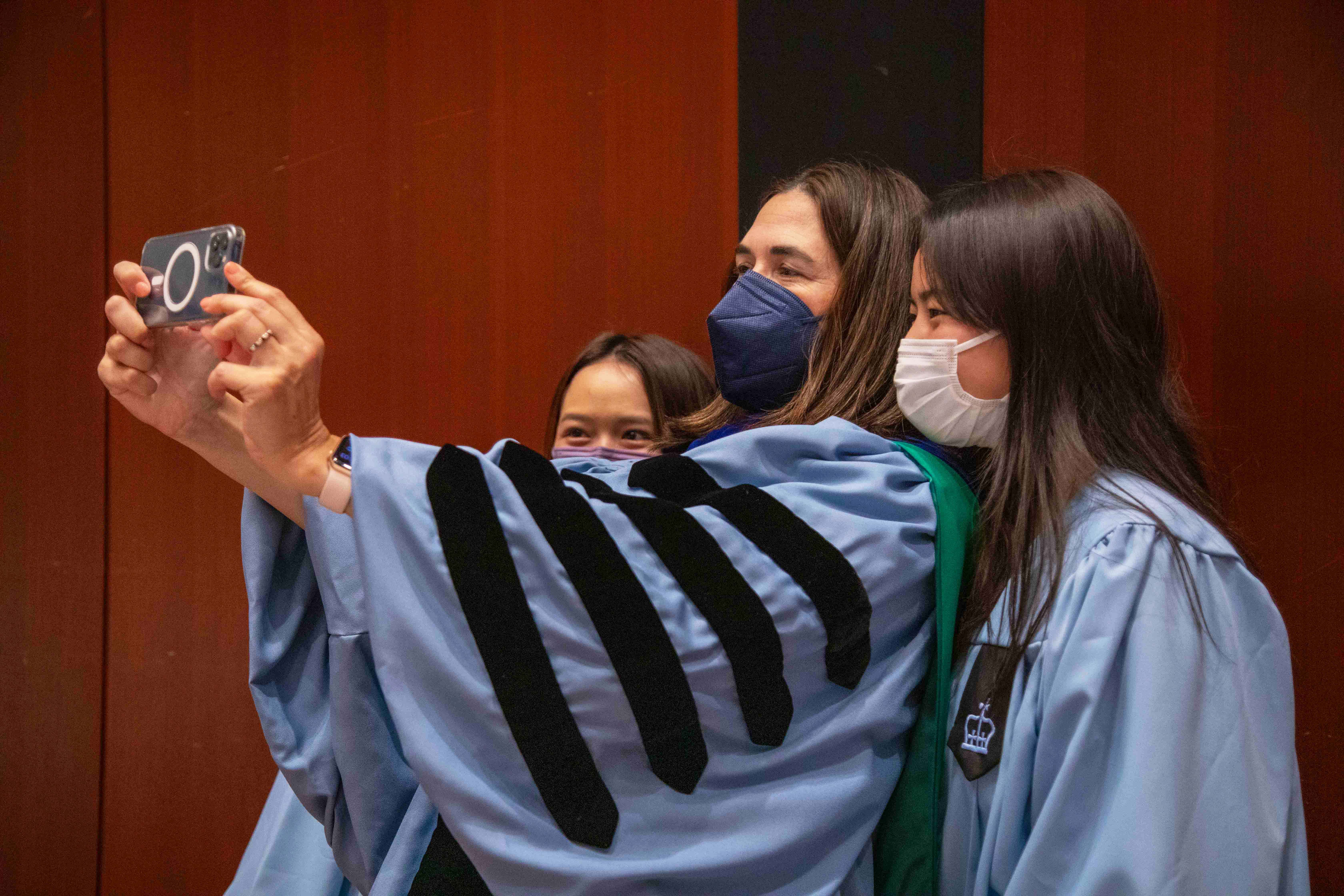 President Beilock holds up an iPhone to take a selfie with two students in their caps and gowns.