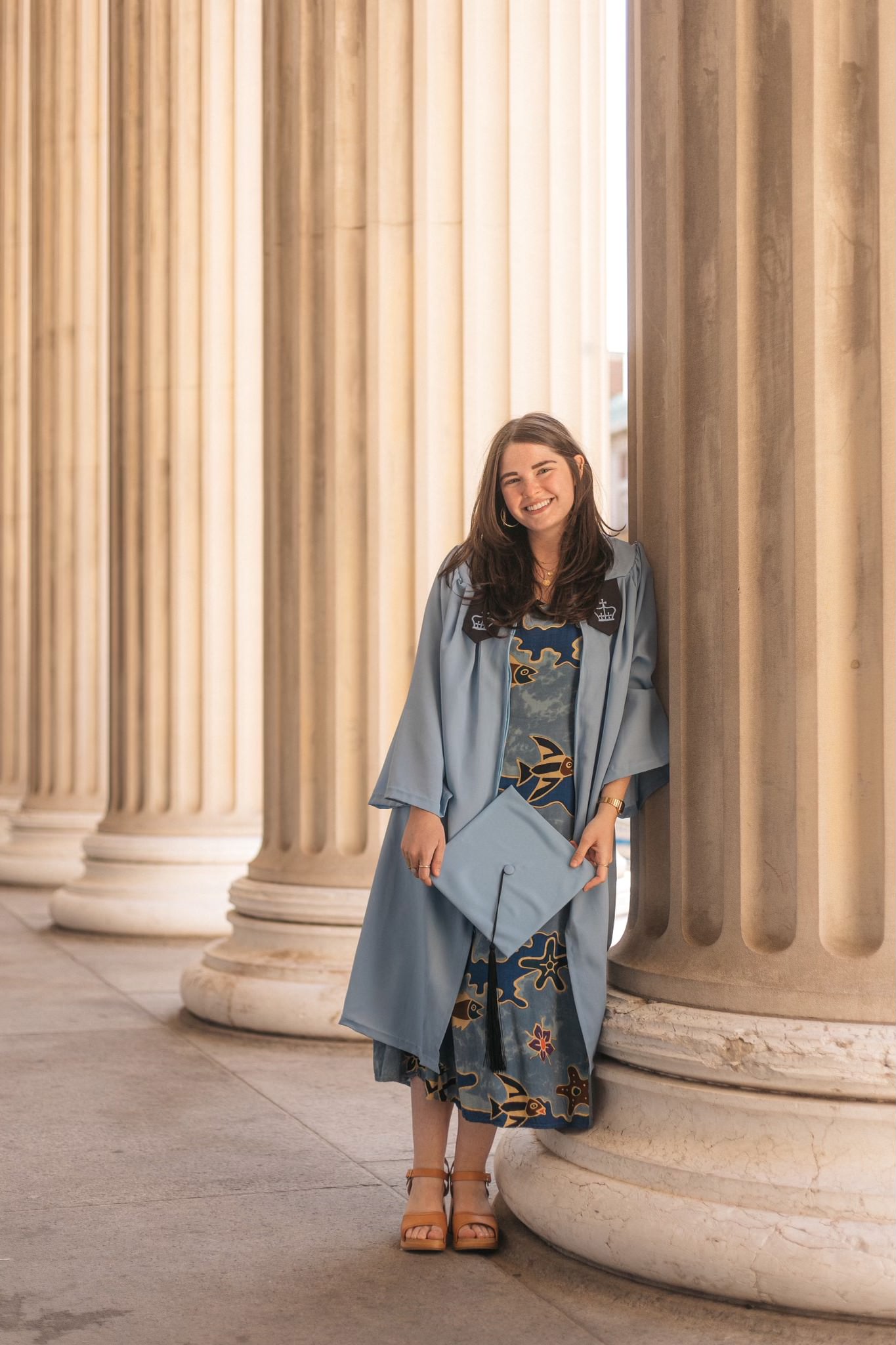 Dani in her cap and gown leading on a large column on Columbia's campus
