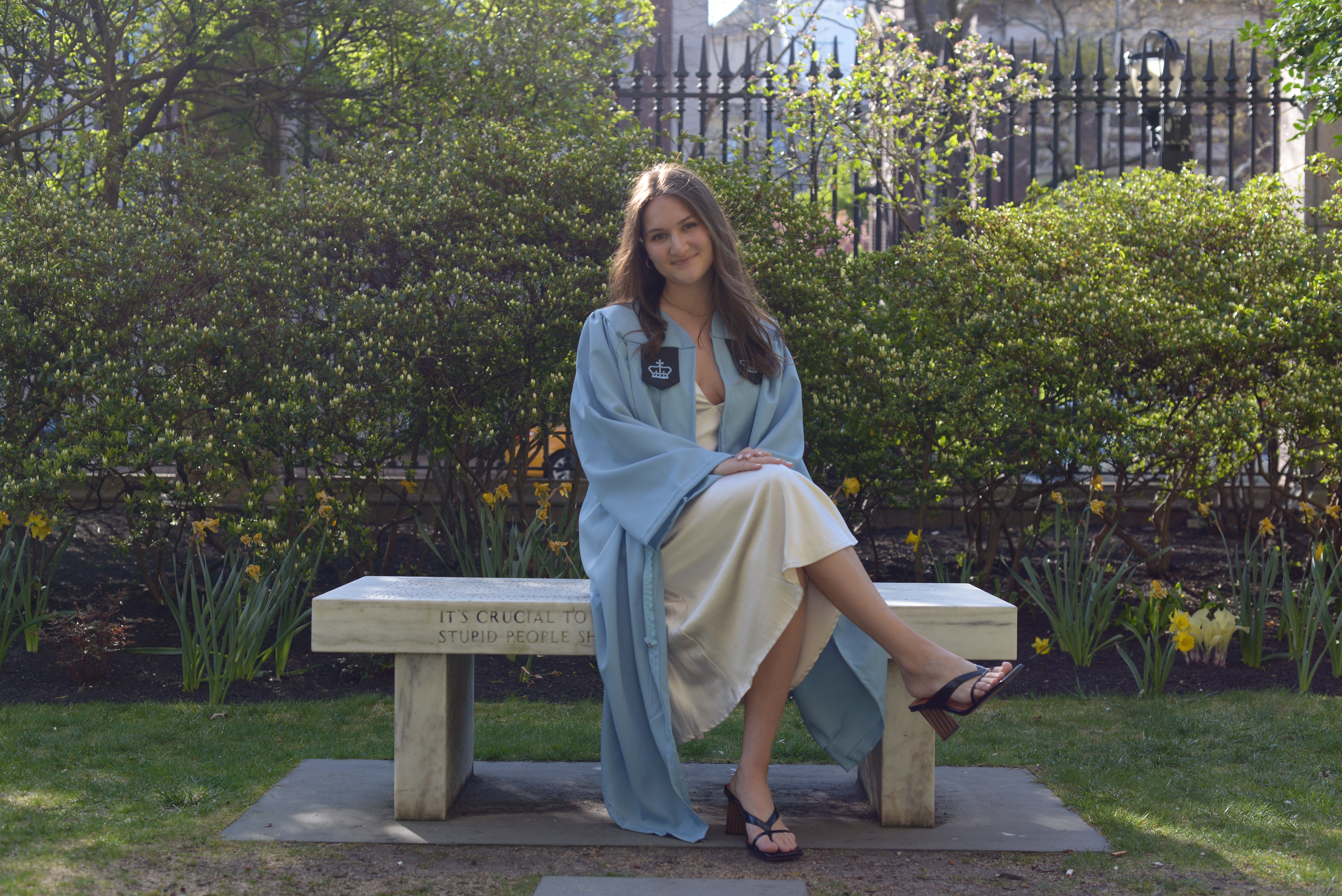 Lucia sitting on a stone bench on Barnard's campus in her cap and gown