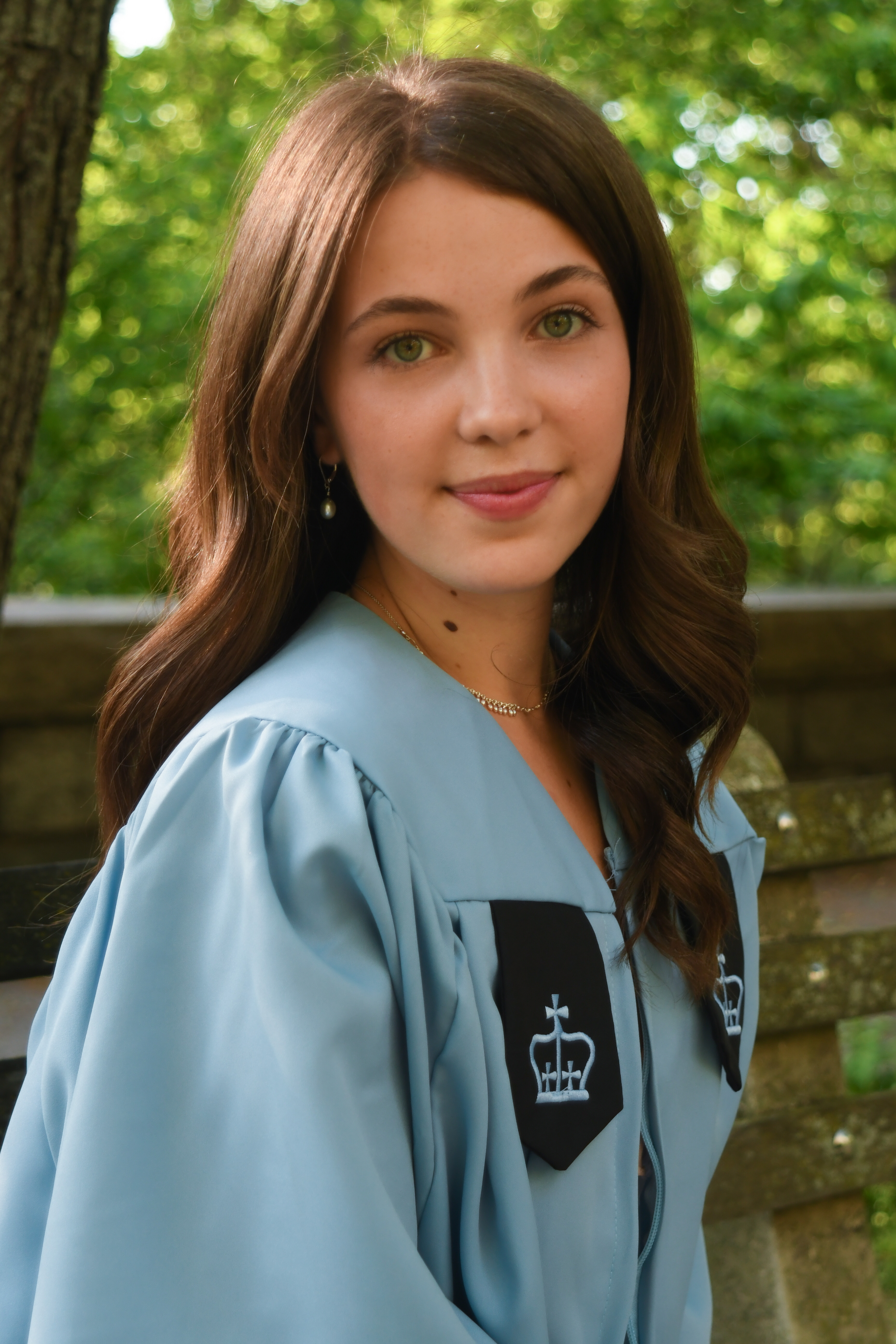 Close-up of Sophia in her graduation gown with greenery behind her