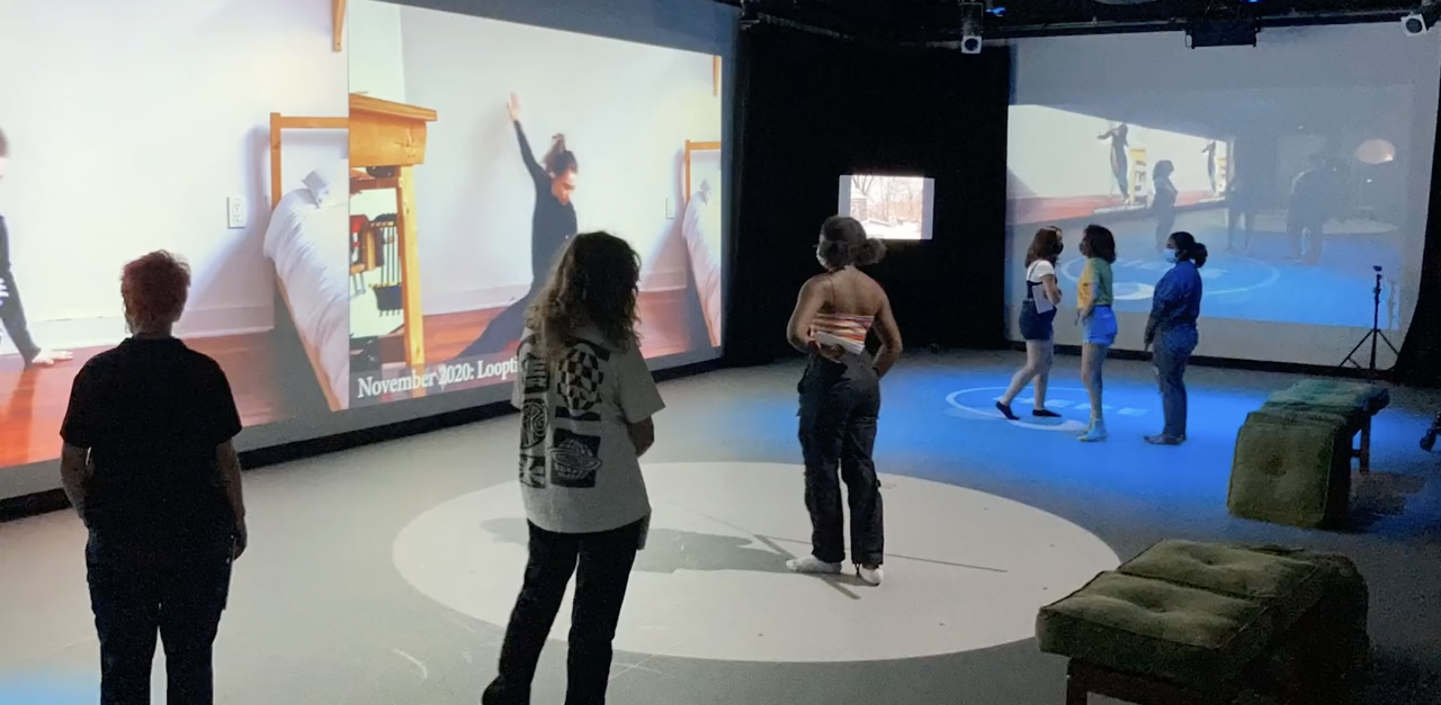 people standing and watching an installation that is projected on the walls and floor of the Movement Lab