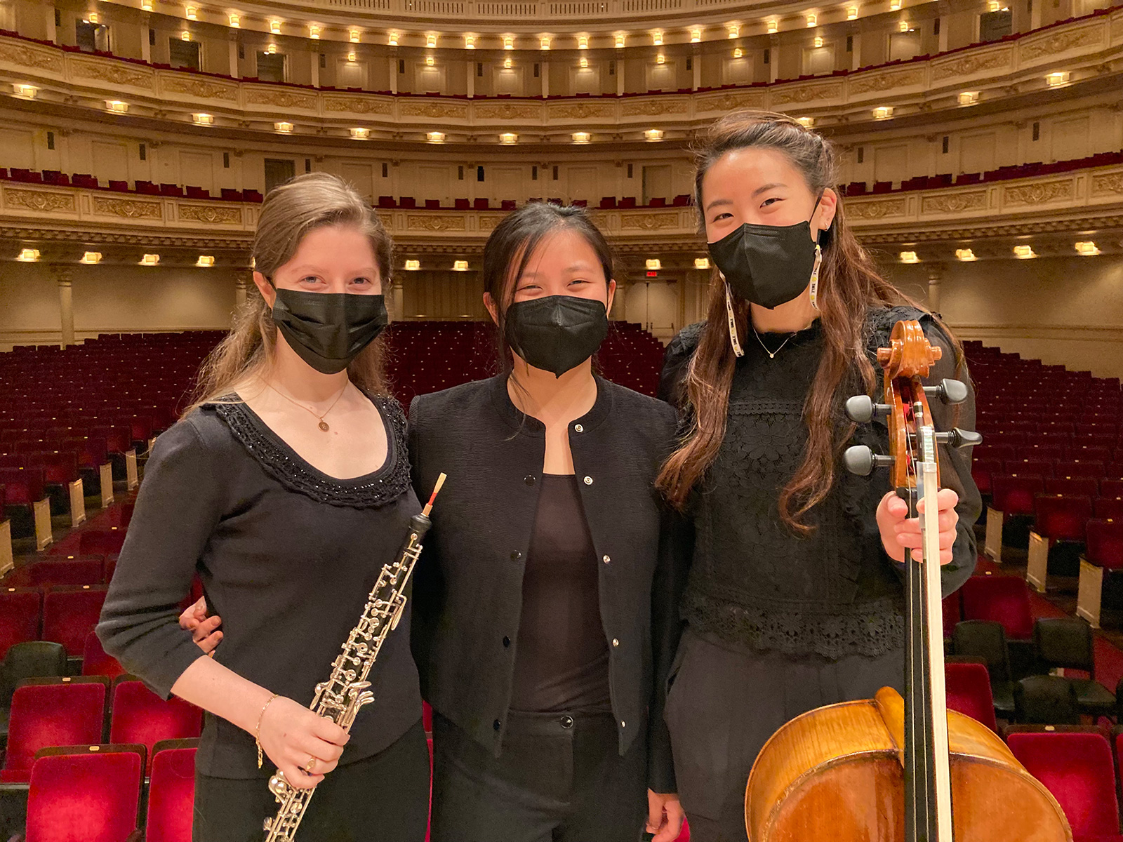 Three women wearing black and masks holding instruments