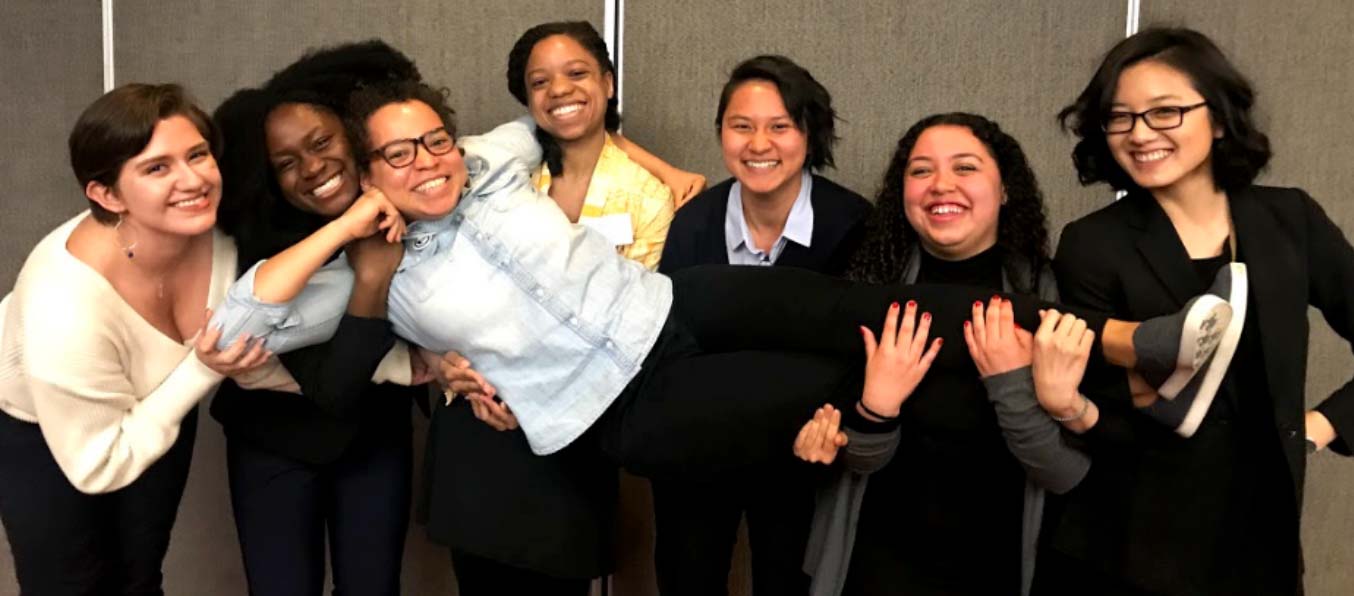6 women of color holding up another one 