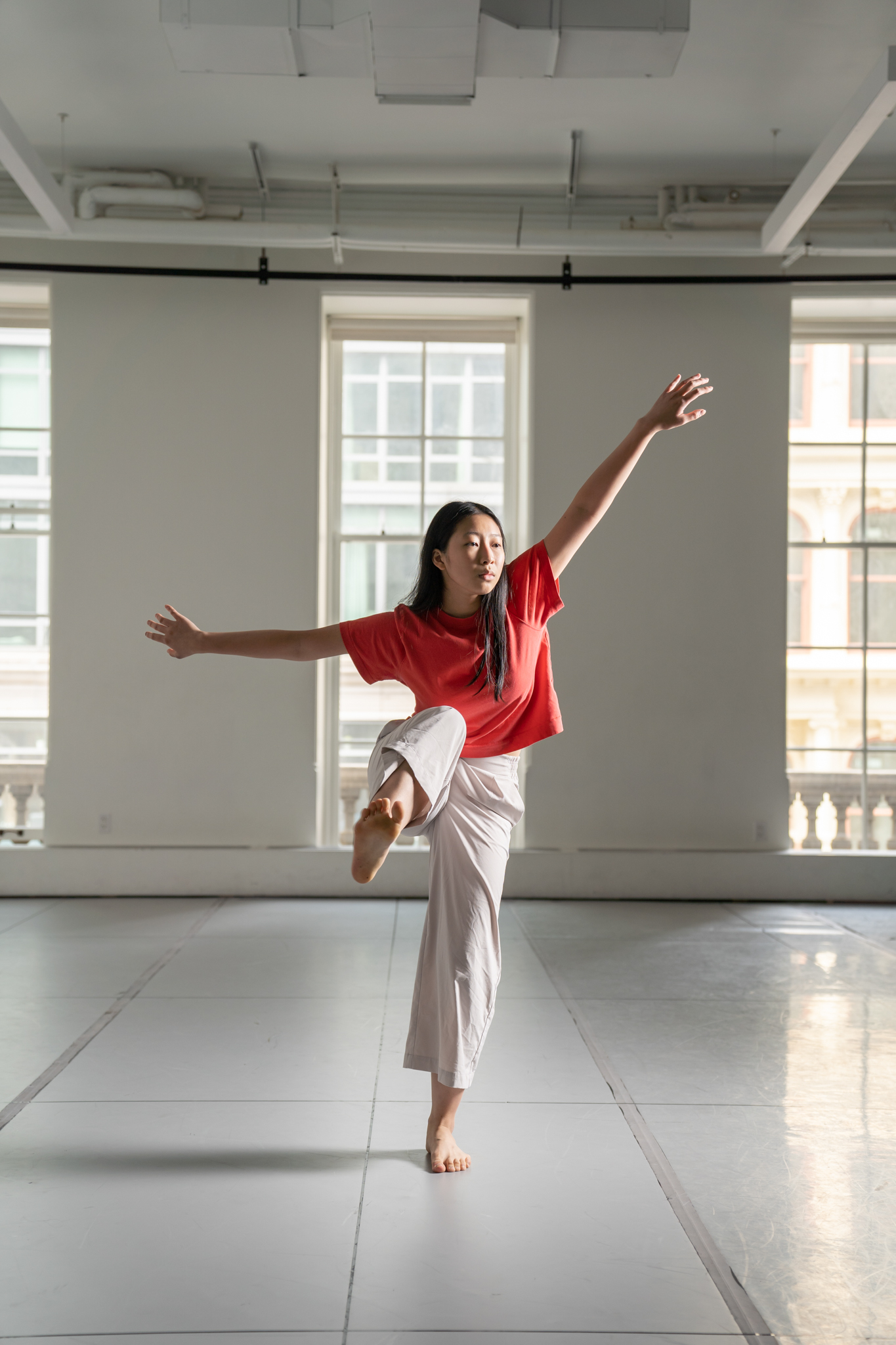 Tobi Lee ’24 in a red shirt and white pants reaching out her arms in a dance pose