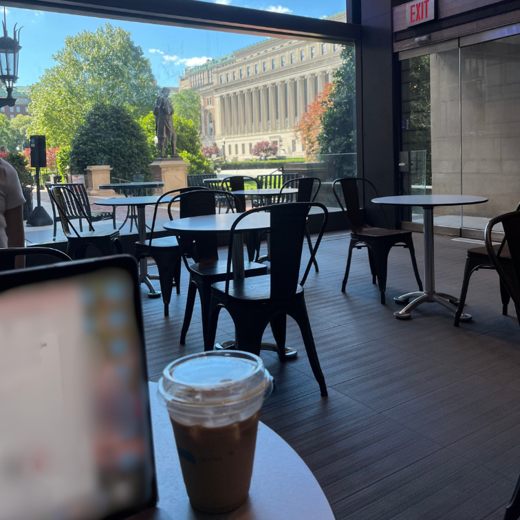 [Image description: A photo of a laptop and an iced coffee. A window with Columbia's campus in the background]