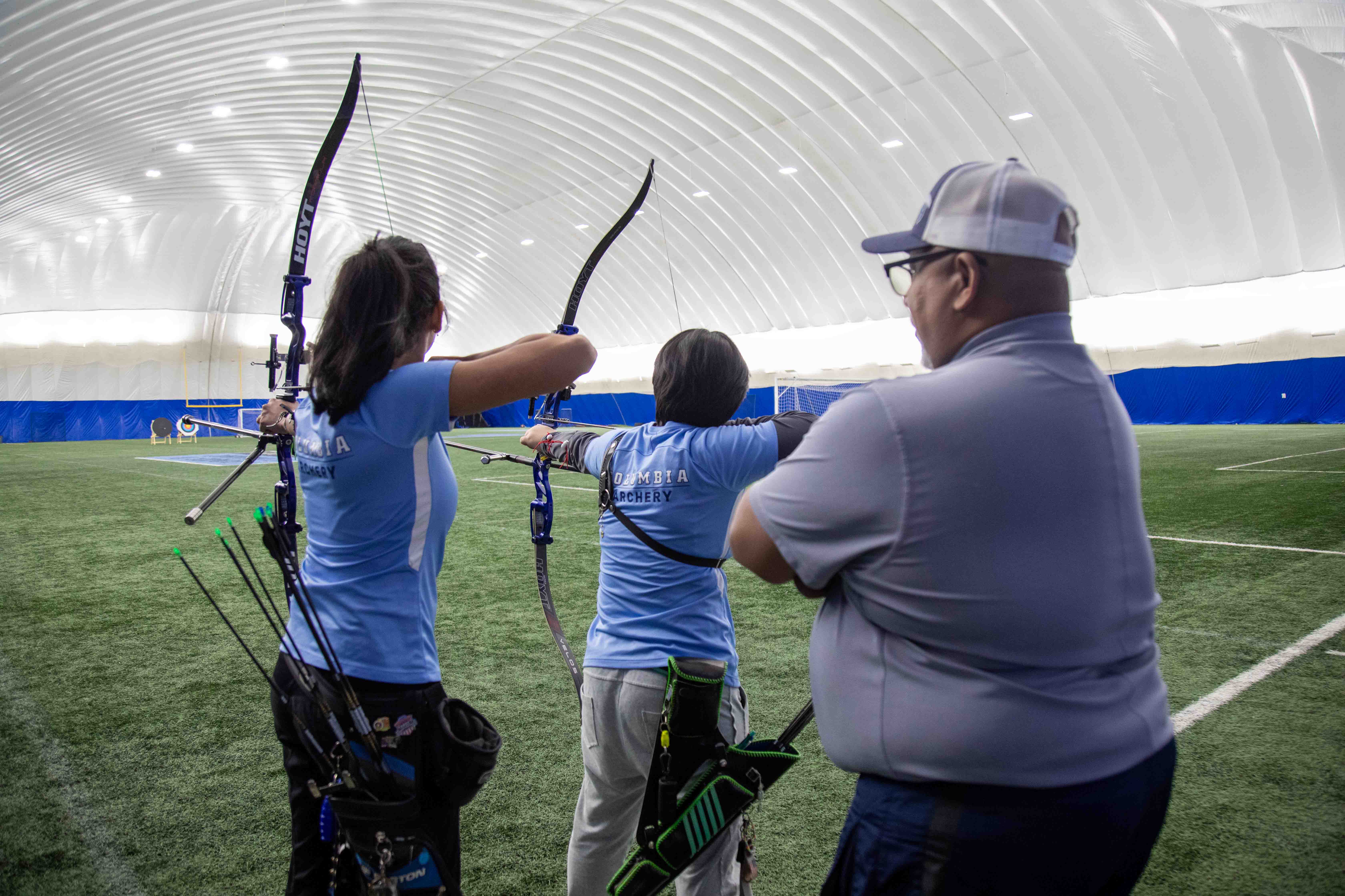 Two women archers practicing in front of man