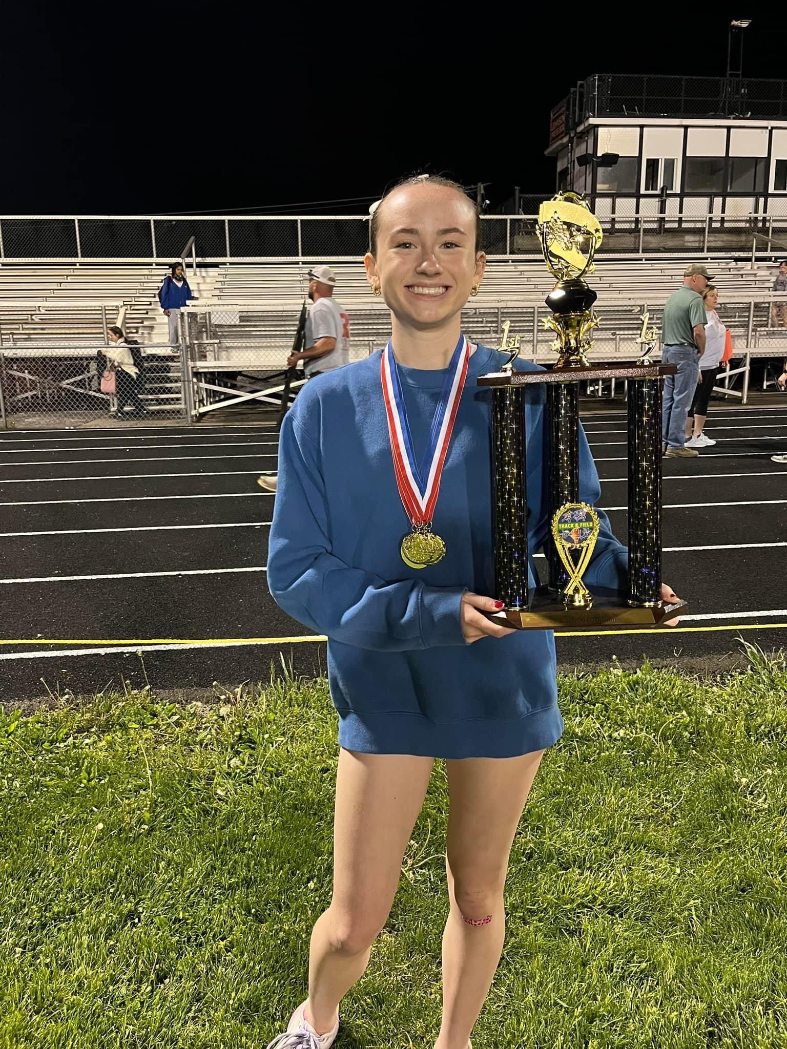 Young woman on track and field wearing blue holding a trophy