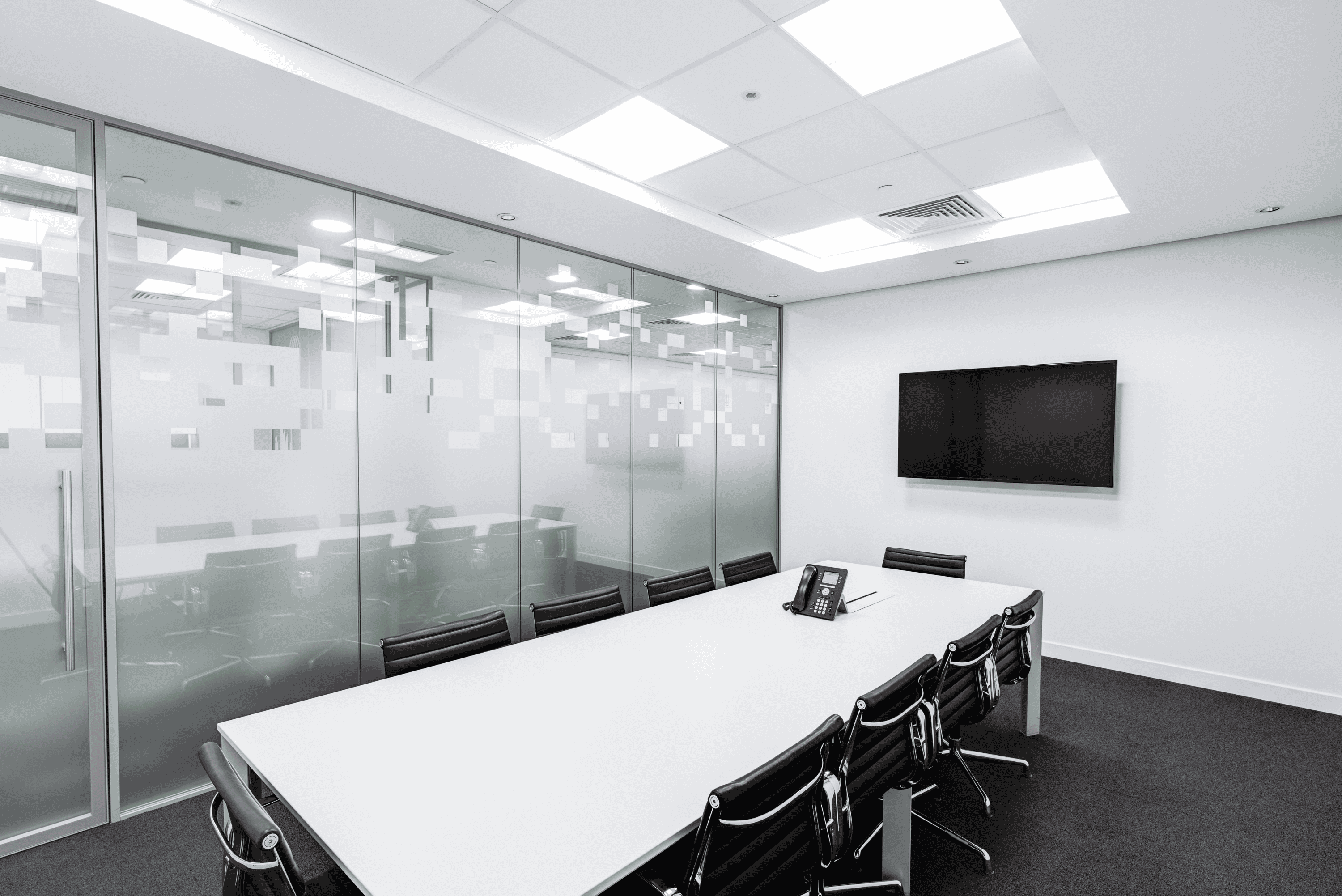 A meeting room resembling a corporate meeting room. The walls and table are white, there is a screen on the wall and a phone on the desk.