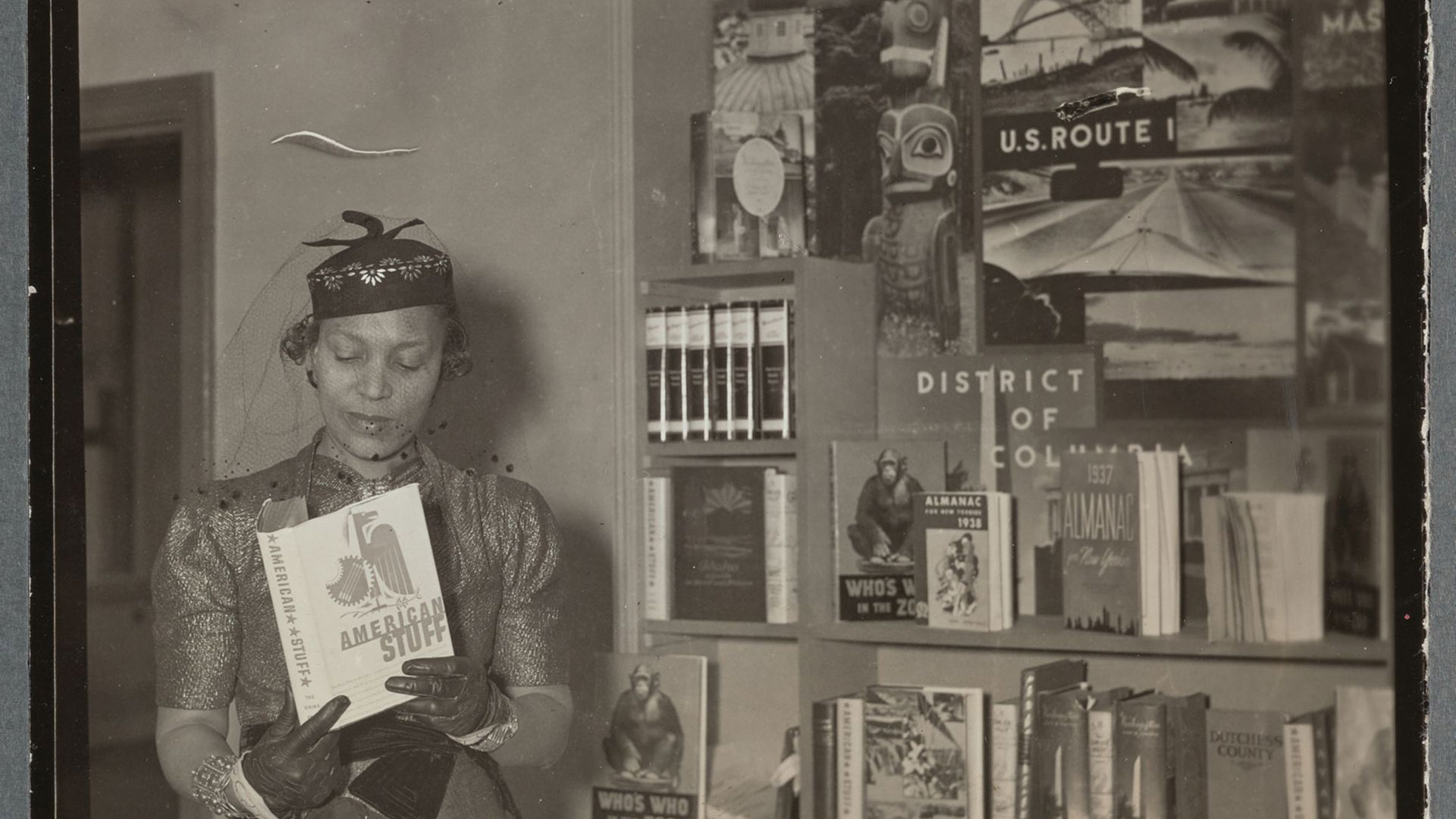 Vintage photo of woman holding up a book and standing in front of. bookshelf