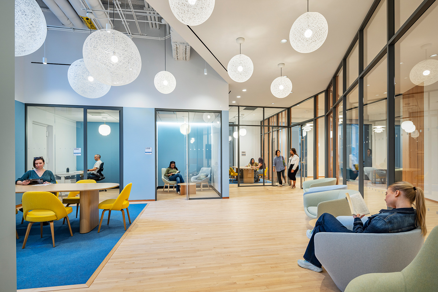 A large windowed office suite is for financial well-being. Students and staff are sitting at tables and lounge chairs working.