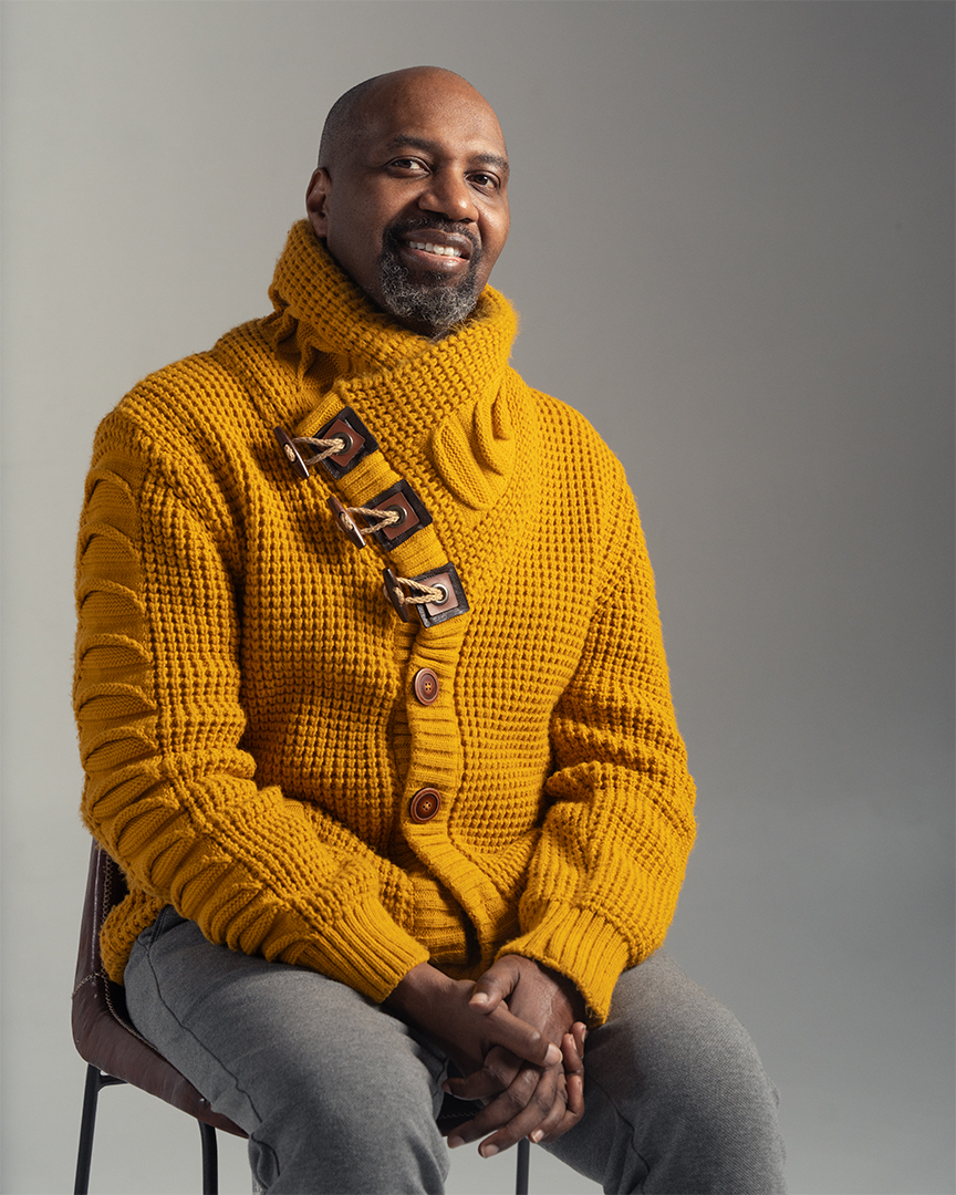 Choreogrpher wearing yellow sweater sitting in chair