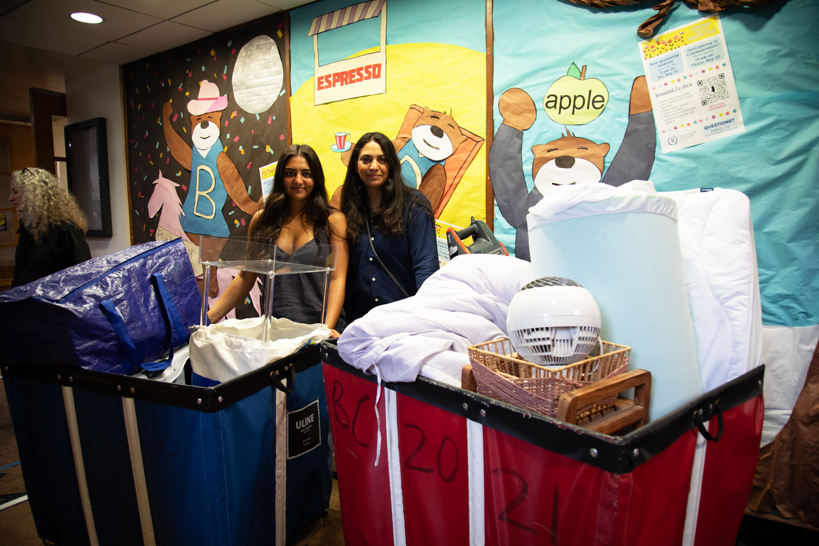 Two women stand in front of big blue and red bins
