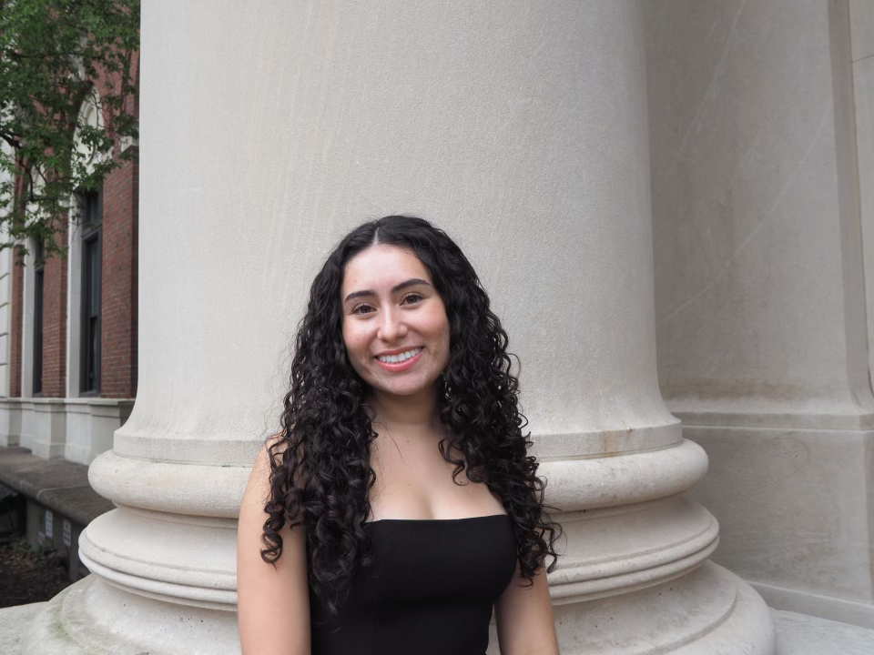 Woman with dark hair and black top standing in front of pillar