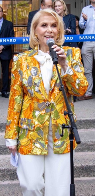 Francine LeFrak in a yellow jacket and white pants holding a microphone in front of Barnard Hall