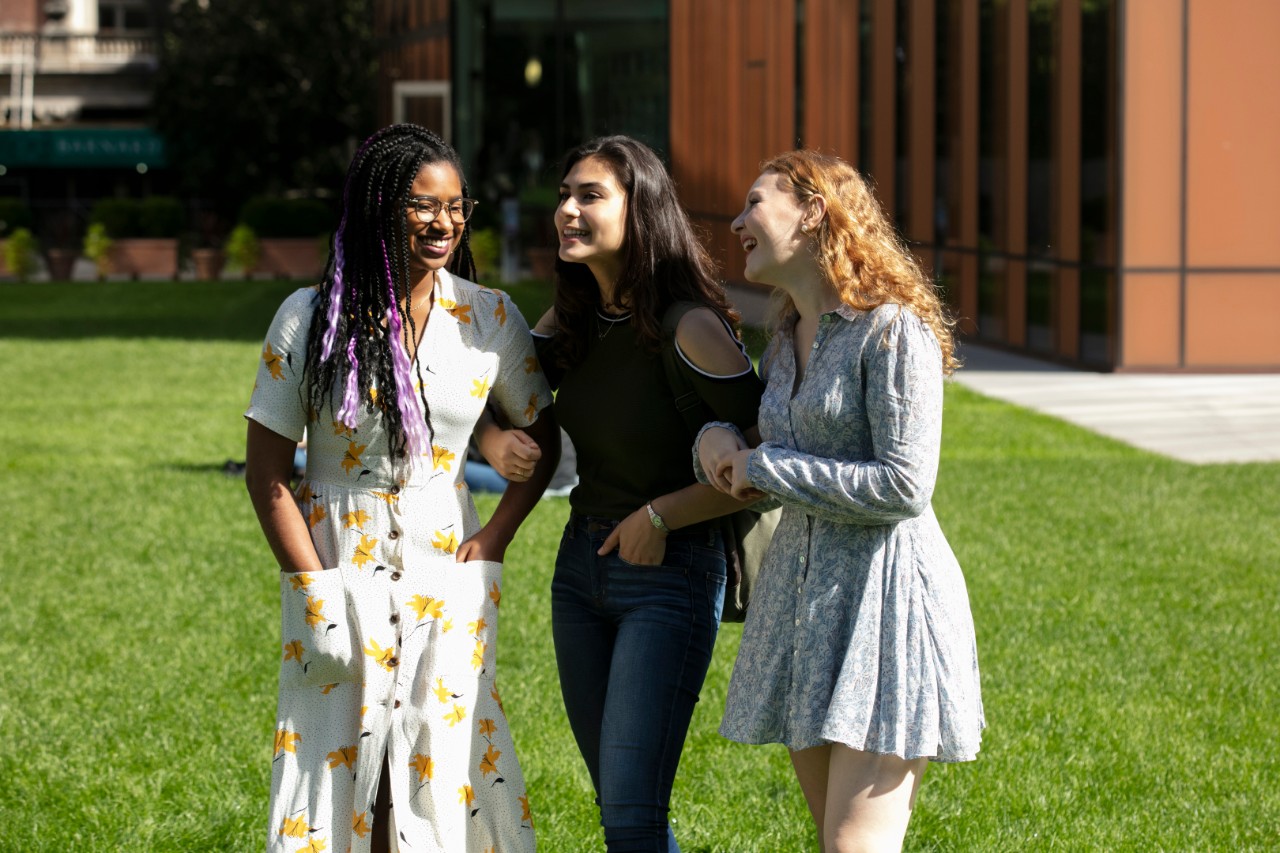 3 young women, arm in arm, crossing campus