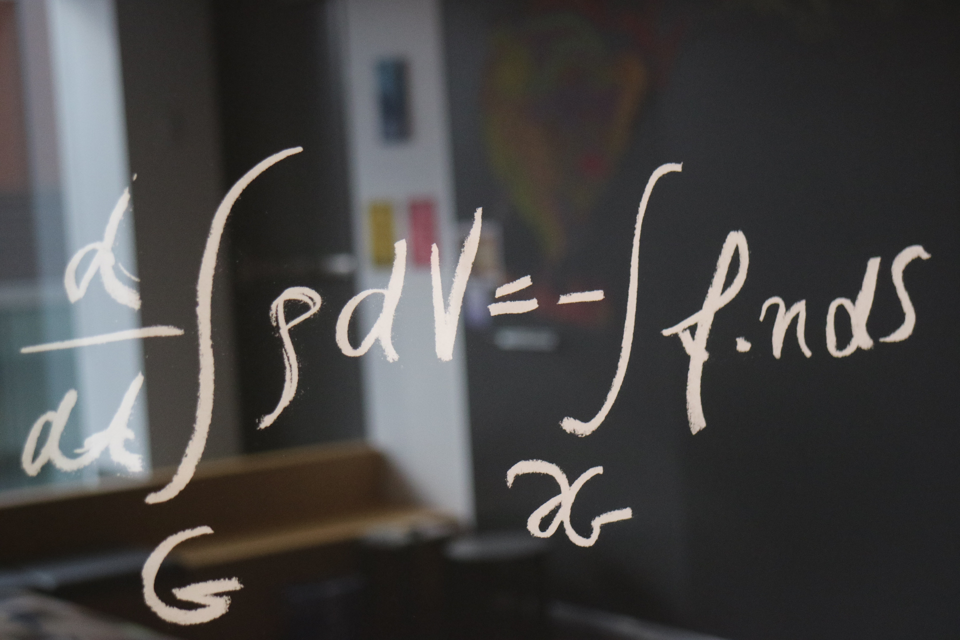 Part of a mathematical formula is written in beige over a blurred image of a dark and light room.