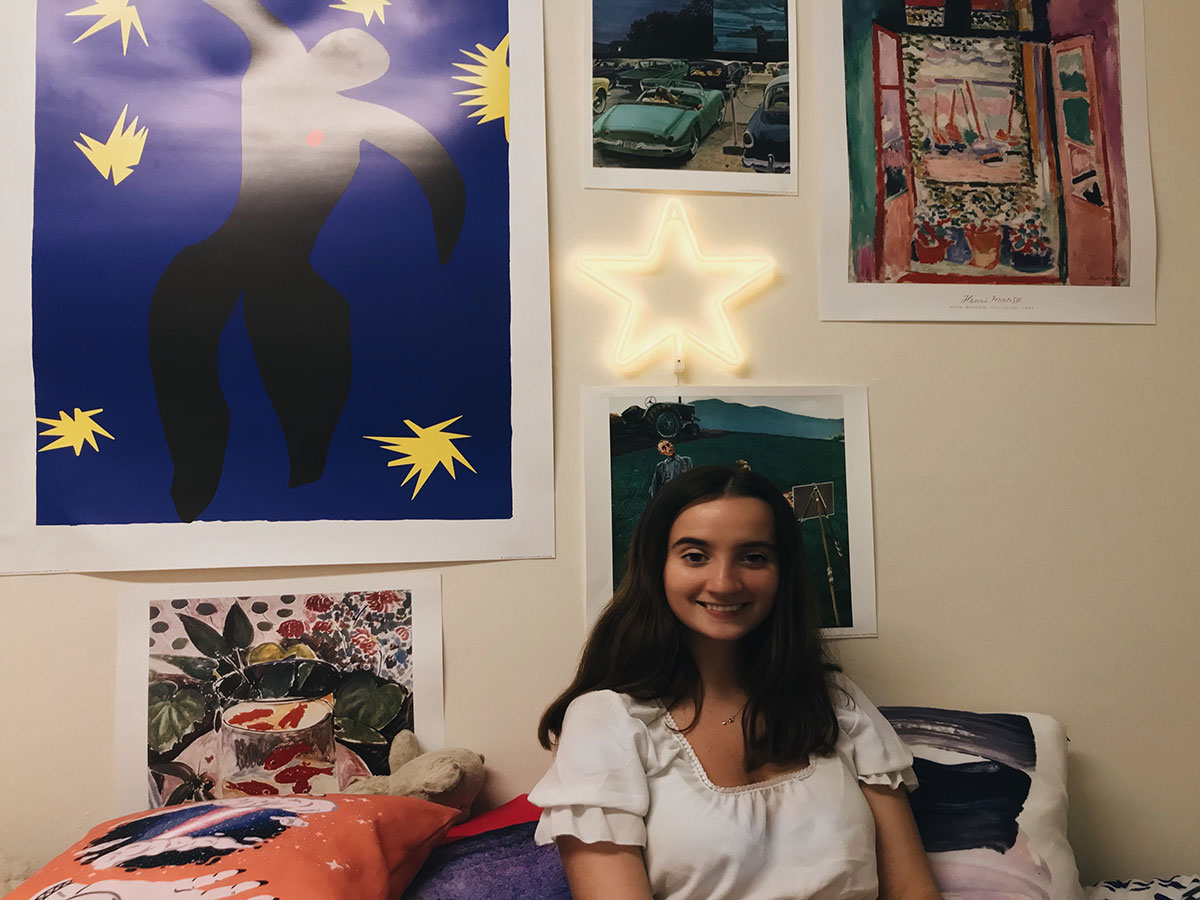 Young women in room with colorful posters behind her on a wall.