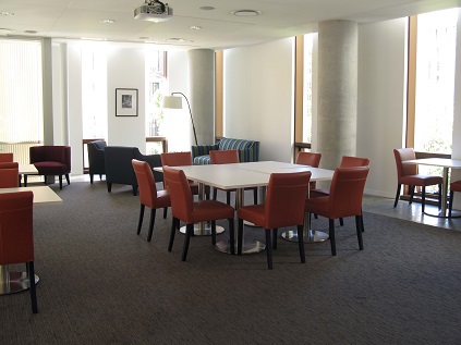 A room with white tables and orange padded chairs set up in the center. Carpet.