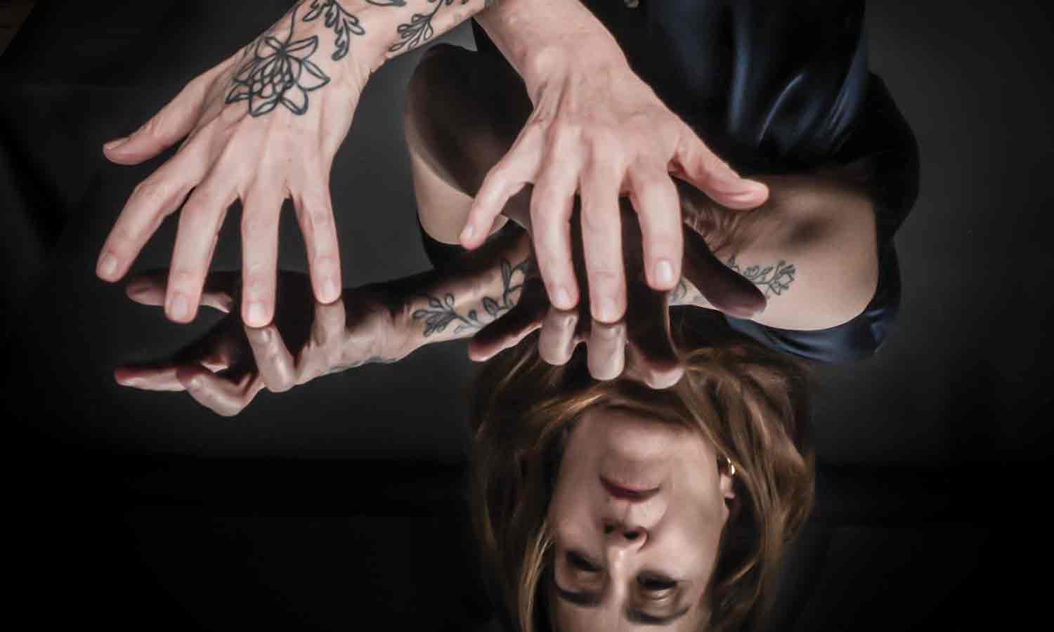 Photo of Jeanine Tesori ’83, her face and tattooed arms and hands reflected in a mirrored tabletop