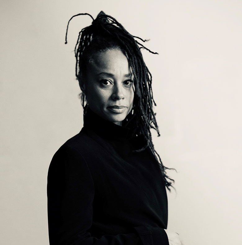 Black woman with long locs wearing dark jacket.