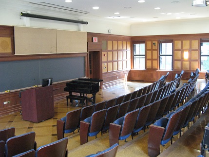 Shows a small tiered lecture hall with wooden floors and built-in seats.