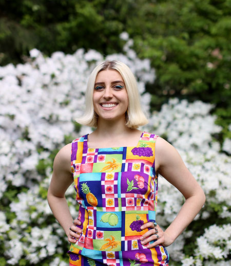 Woman with ice blonde shoulder-length straight hair, wearing graphic print dress.