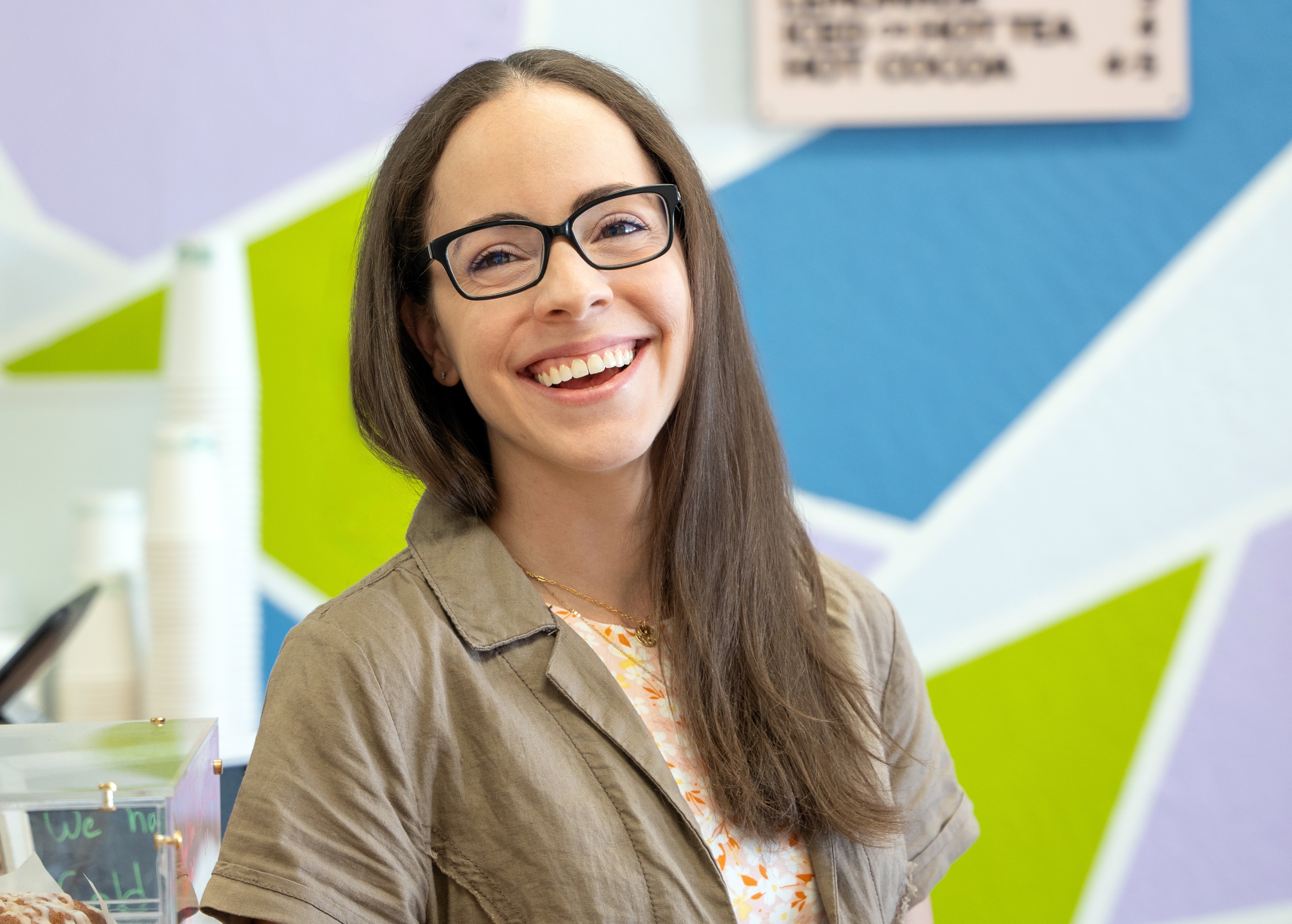 Woman in glasses smiling against bright background.