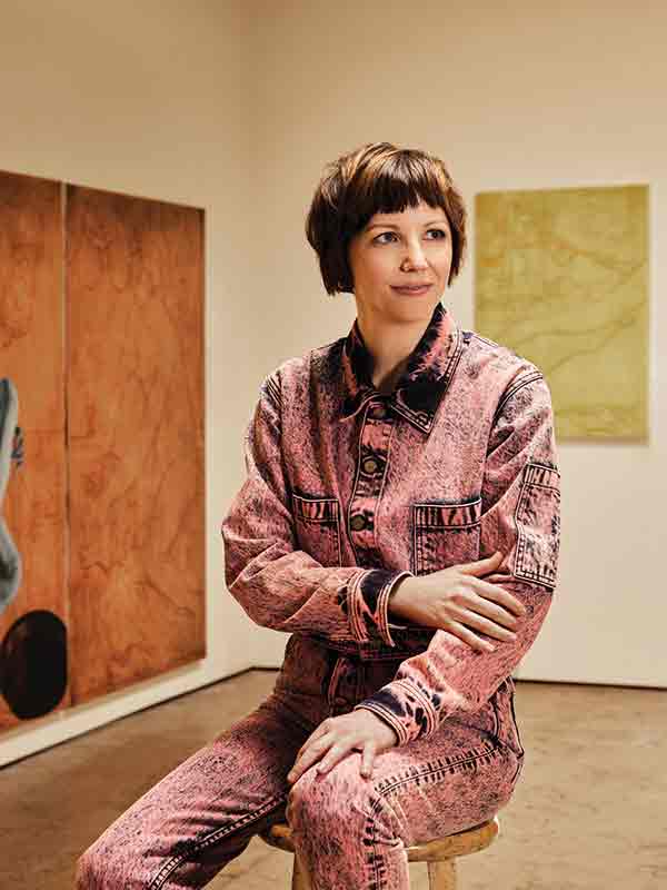 Jesse Mockrin sitting on a stool in an art gallery wearing a dark-pink denim outfit