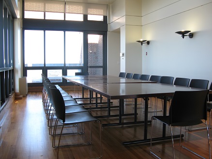 picture showing wooden floors and tall ceilings with floor-to-ceiling glass, set with a long wooden table with black chairs.