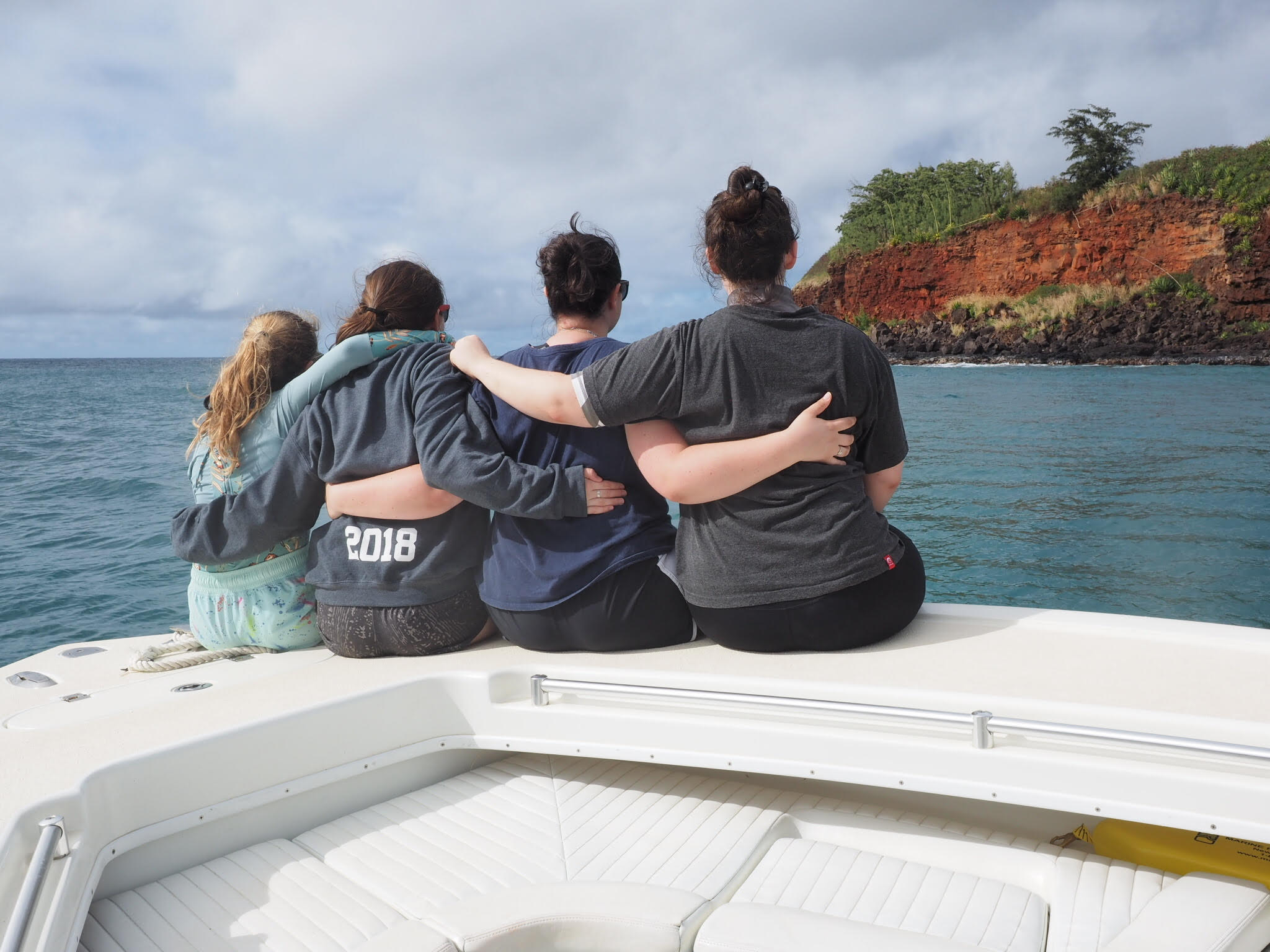 Ellie Harrison and her three sisters sitting on a boat with their backs to the camera.