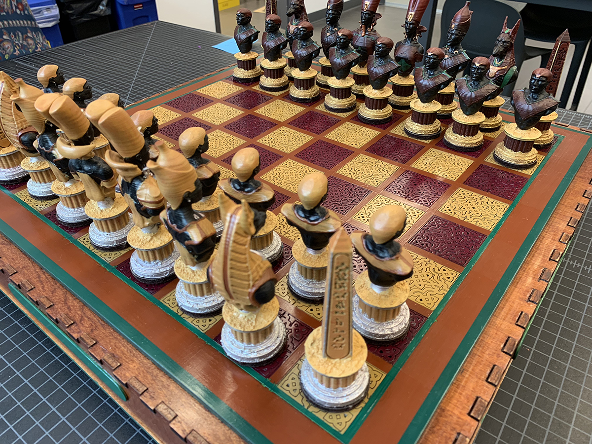A chess set with pale yellow and burgundy squares on the board. The chess pieces are shaped like historical Egyptian figures.