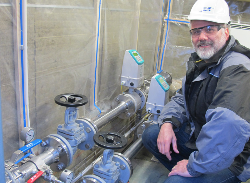 Martin Stute squats next to several large pipes and valves